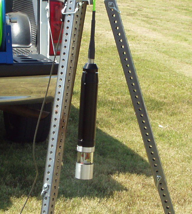 Reel Hose Nozzle Hanging From a Metal Stand on a Grassy Field