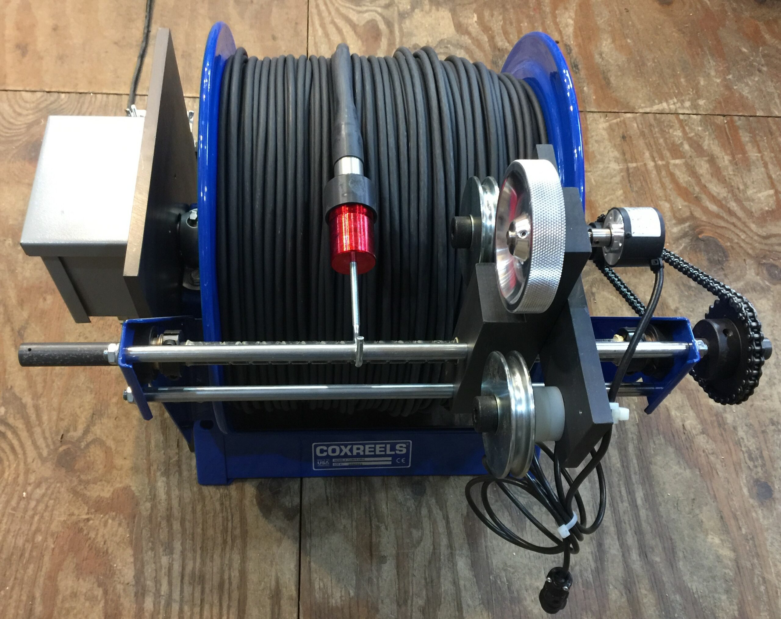Blue Hose Reel With a Black Hose and a Handle on a Wooden Floor